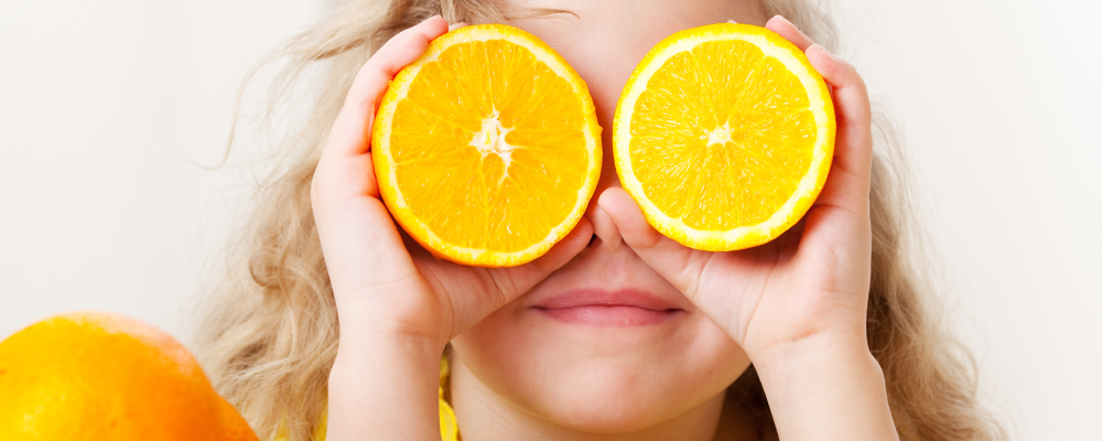 Young girl holding up two orange slices over her eyes like googles.