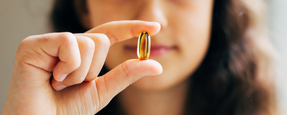 Young girl holding a fish oil pill between her fingers